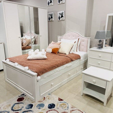 White bedroom set with bed, nightstands, and mirror in a showroom setting.